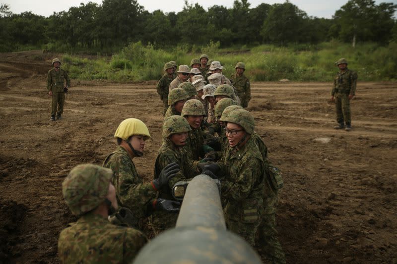 Marines estadounidenses y fuerzas de defensa japonesas en terreno limpian partes de un tanque japonés