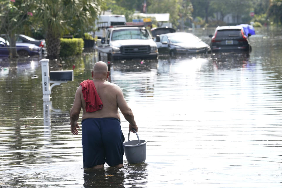 A man walks with a bucket on a flooded street, Friday, April 14, 2023, in Fort Lauderdale, Fla. South Florida has begun draining streets and otherwise cleaning up after an unprecedented storm that dumped upward of 2 feet of rain in a matter of hours. (AP Photo/Marta Lavandier)