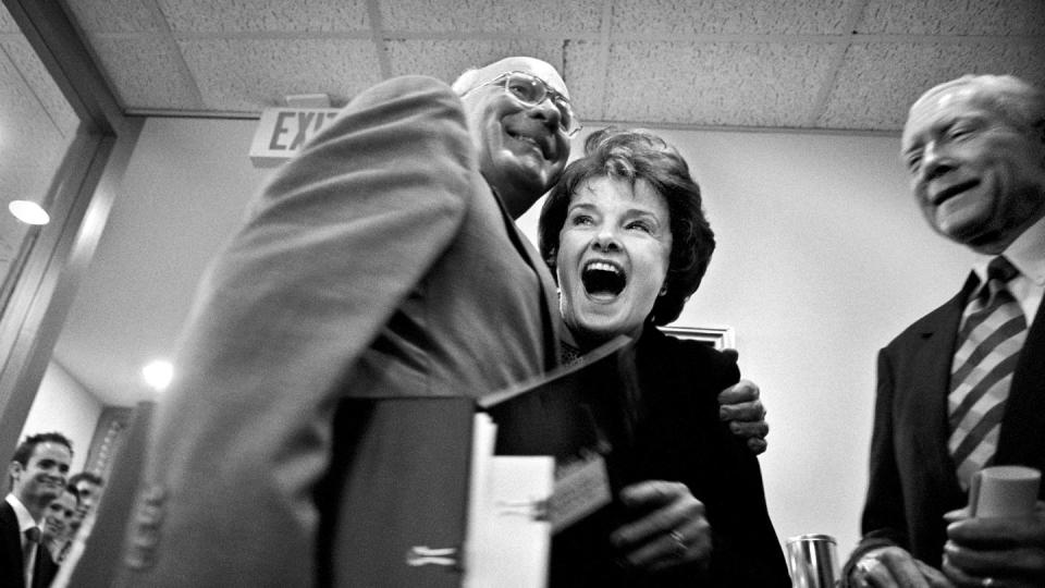 patrick leahy hugging a laughing dianne feinstein as both hold binders, with orrin hatch standing next to them and smiling