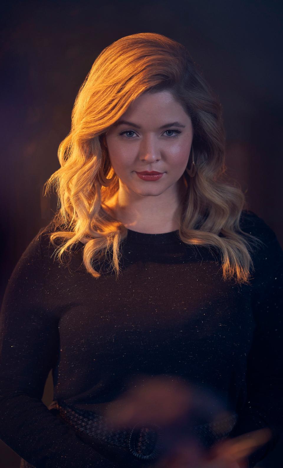 Sasha Pieterse poses in a dark, long-sleeved outfit, looking directly at the camera with a slight smile