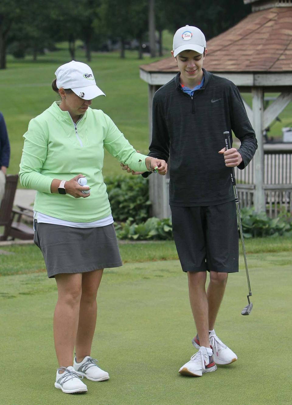 Huston Nagy, 16, of North Olmsted, who is blind, is assisted by coach Erin Craig to the spot where he will putt on the putting green at Firestone Country Club on Monday in Akron.