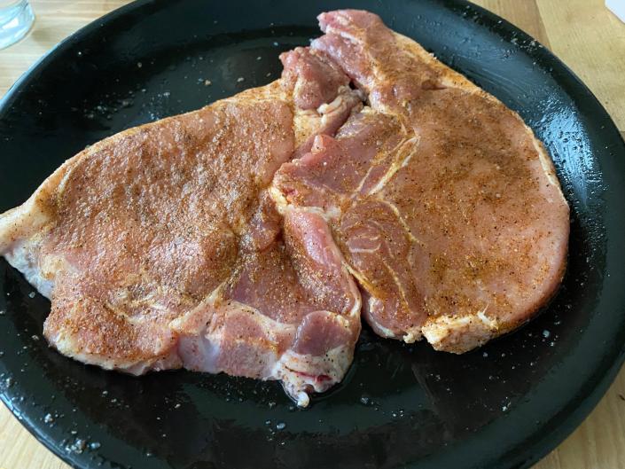 A photo of raw seasoned pork chops on a plate