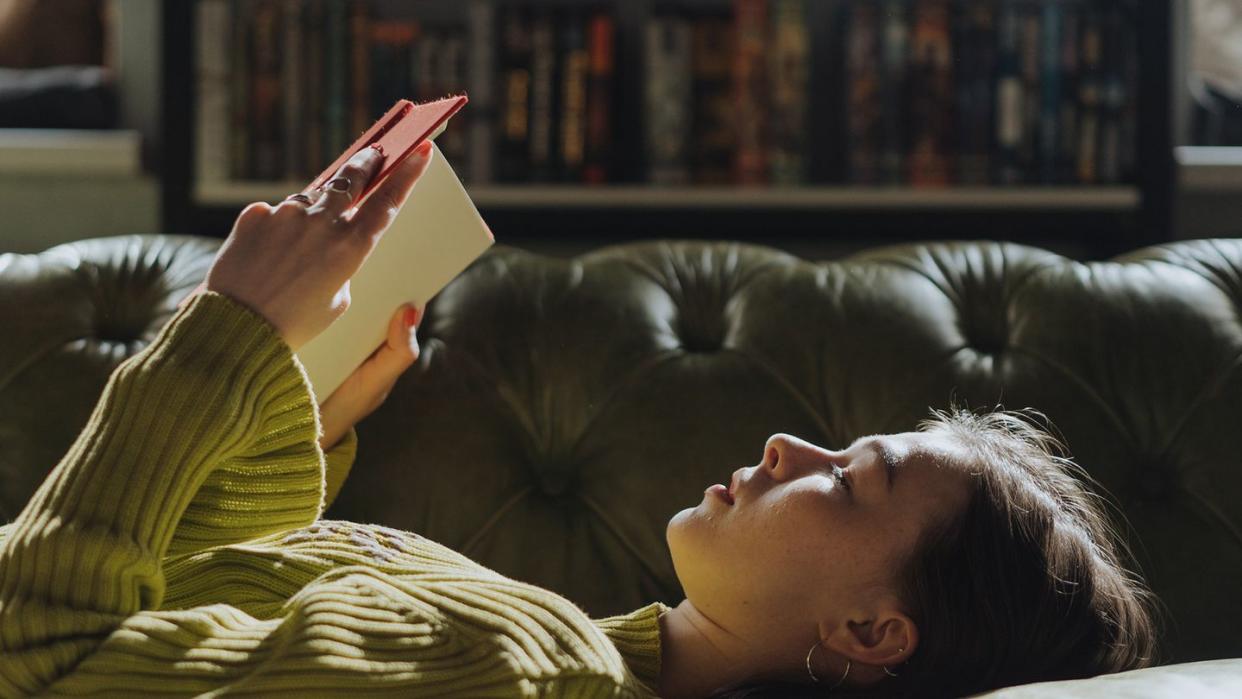 a person lying on a couch reading a book