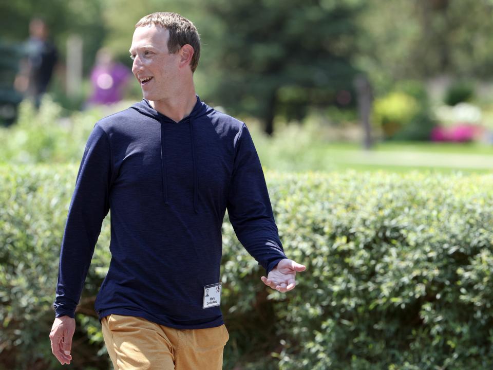 Mark Zuckerberg wearing a name badge and walking past a hedgerow in a park.