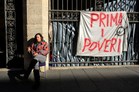 Angela Grossi sits next to a banner reading "Poor first", hanging in a gate of the portico of the Basilica of the Santi Apostoli, where she lives after being evicted from an unused building along with other families in August 2017, in Rome, Italy January 29, 2018. REUTERS/Tony Gentile