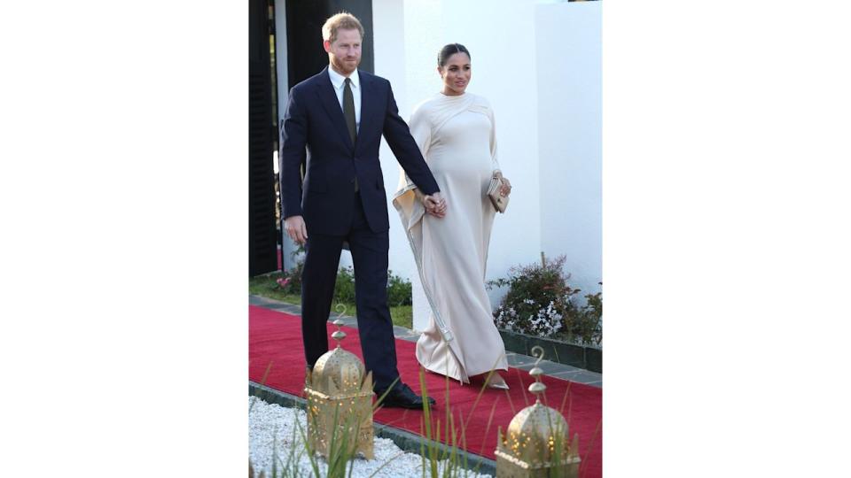 Prince Harry in suit walking with Meghan in ivory caped dress