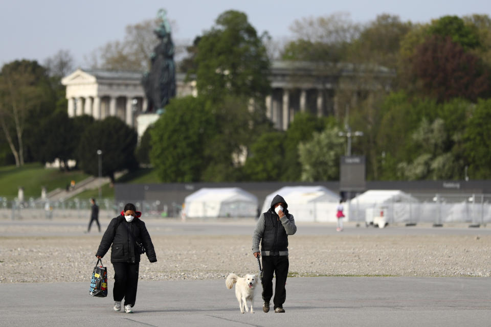 People wearing protection masks as they across the 'Theresienwiese', the Oktoberfest beer festival area, in Munich, Germany, Tuesday, April 21, 2020. Bavarian state governor Markus Soeder and Munich mayor Dieter Reiter announced at a news conference that the Oktoberfest is cancelled this year because the coronavirus outbreak. (AP Photo/Matthias Schrader)