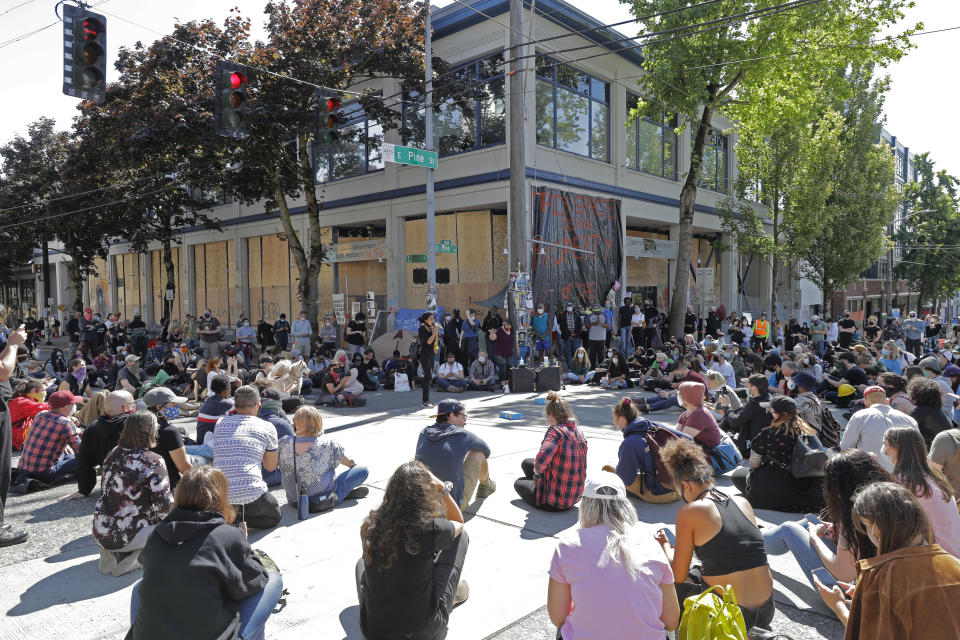 Protesters listen to a speaker as they sit in front of the Seattle Police Department East Precinct building, which has been boarded up and abandoned except for a few officers inside, Thursday, June 11, 2020, inside what is being called the "Capitol Hill Autonomous Zone" in Seattle. Following days of violent confrontations with protesters, police in Seattle have largely withdrawn from the neighborhood. (AP Photo/Ted S. Warren)