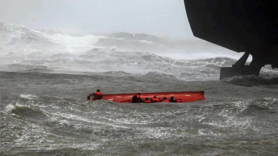 Sailors try to hold on to their up-turned lifeboat, as sailors, not pictured, throw lines to them from the ship above, after the lifeboat capsized when Indian ship Pratibha Cauvery, right, ran aground, due to strong winds in the Bay of Bengal coast in Chennai, India, Wednesday, Oct. 31, 2012. More than 100,000 people were evacuated from their homes Wednesday as a tropical storm hit southern India from the Bay of Bengal, officials said.(AP Photo) INDIA OUT