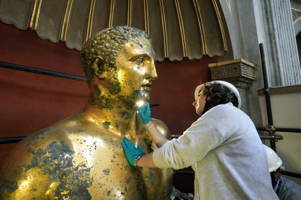 Vatican Museum restorer Alice Baltera works on the bronze Hercules statue, in the Round Hall of the Vatican Museums, Thursday, May 11, 2023. Work will continue until December to reveal the 4-meter- (13-foot-) tall Hercules, believed to have stood in ancient Rome’s Pompey Theater, to its original golden sheen. The discovery of the gilded bronze in 1864 during work on a banker’s villa near Piazza dei Fiori made global headlines. (AP Photo/Andrew Medichini)