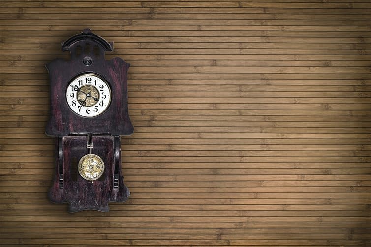 An old pendulum clock with a wooden wall behind.