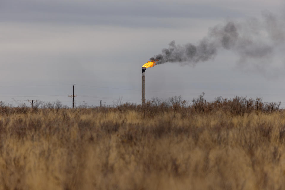 A natural gas flare stack belches black smoke in scrubland.