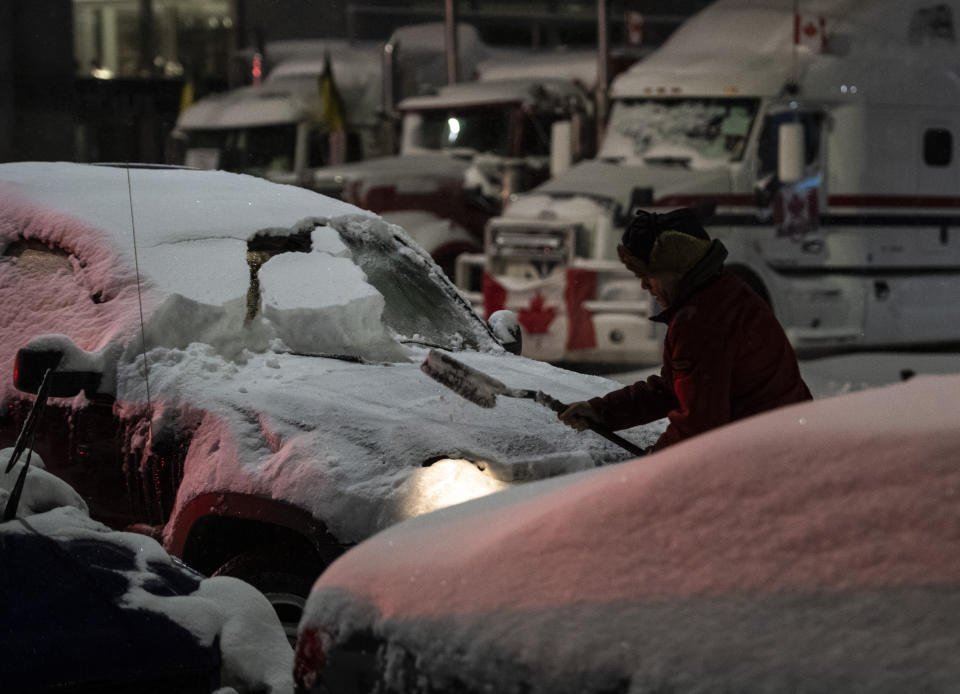 A person brushes snow off their car beside a blockade of trucks, as a winter storm warning is in effect, during a protest against COVID-19 measures in Ottawa, on Friday, Feb. 18, 2022. (Justin Tang /The Canadian Press via AP)