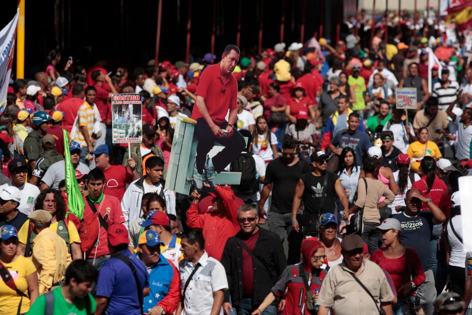 Un hombre sostiene un afiche con la imagen del presidente venezolano Hugo Chávez, ya fallecido, en medio de una multitud de partidarios gubernamentales que aguardan la llegada del mandatario Nicolás Maduro en Caracas, Venezuela, el sábado 22 de marzo de 2014. (Foto AP/Esteban Félix)