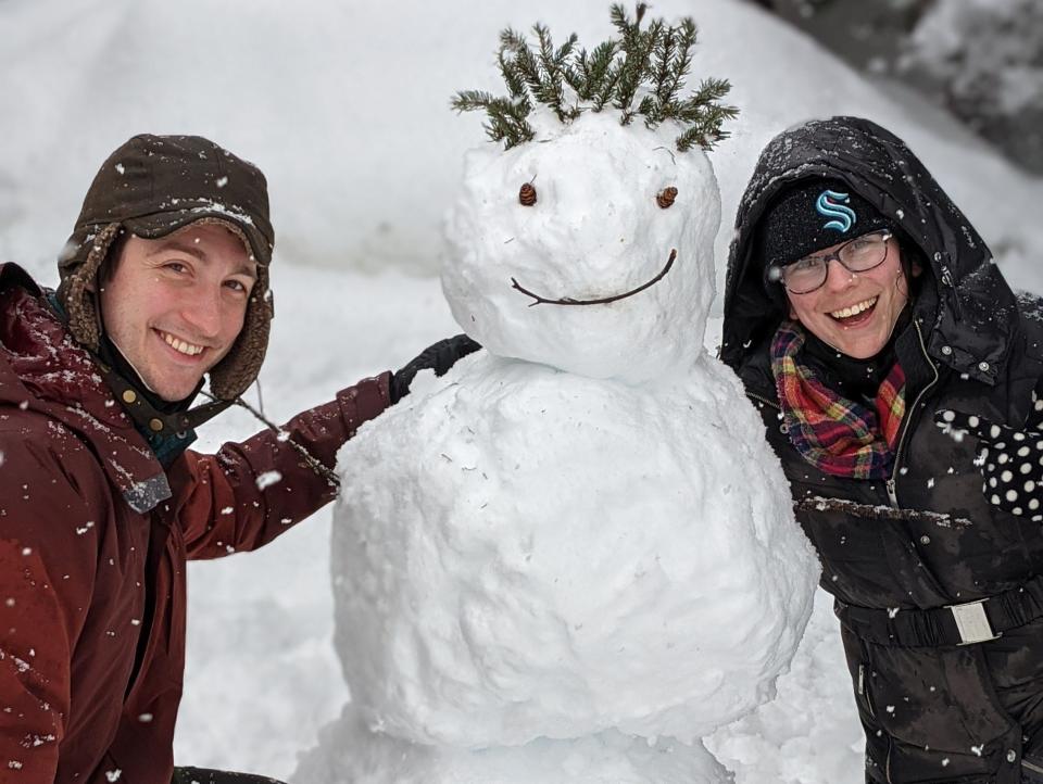 Abby and her partner posing in heavy jackets with a snowman in Alaska