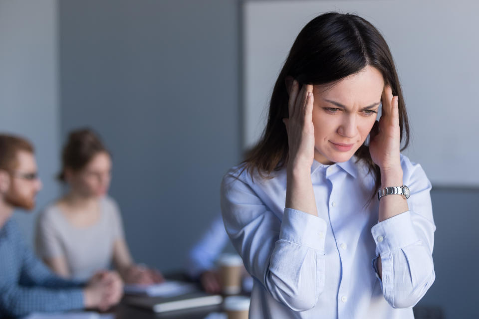 Stressed millennial woman suffer from headache during team business meeting, tired or frustrated female employee feel migraine or dizziness, not able to focus on work, worker avoiding loud voices