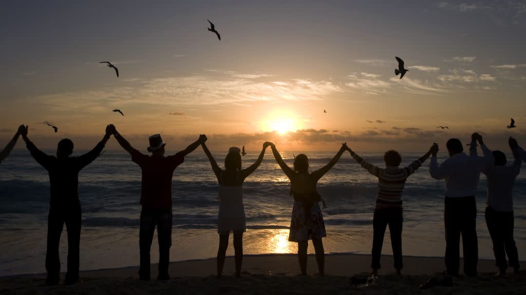 People raise their arms to welcome the first rays of sunshine of the new year on Playa Delfin in Cancun, Mexico