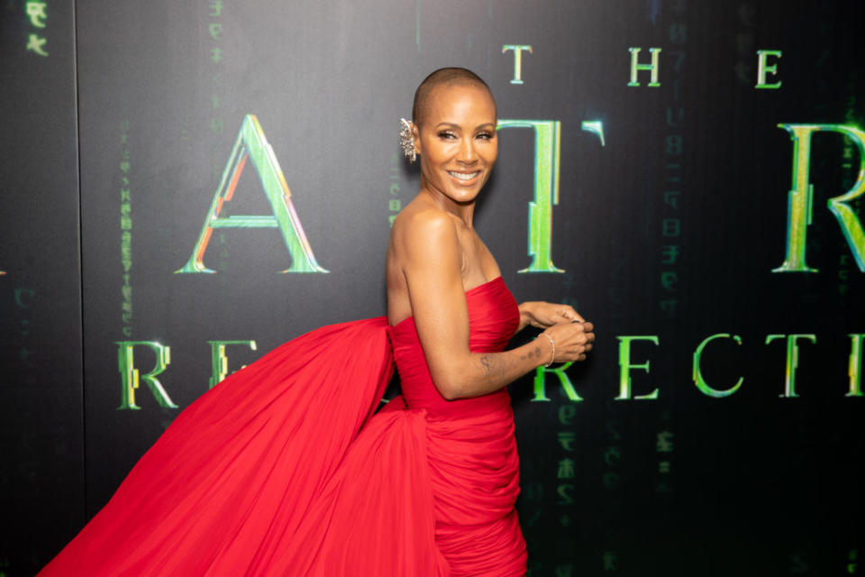 Jada Pinkett-Smith posing on the red carpet for the Matrix Resurrections in a strapless gown and rocking a shaved head
