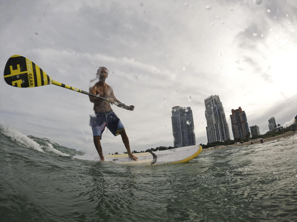 Graziano La Grasta, a local contractor and standup paddle board enthusiast, rides a small wave off South Beach, Friday, July 28, 2023, in Miami Beach, Fla. Humans naturally look to water for a chance to refresh, but when water temperatures get too high, some of the appeal is lost. (AP Photo/Rebecca Blackwell)