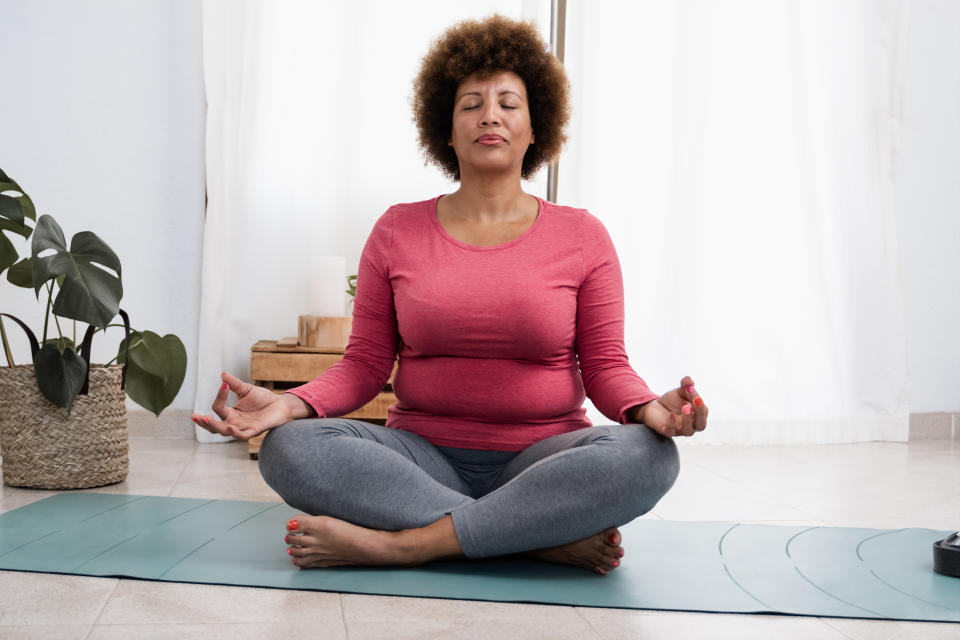 African senior woman doing pranayama breath exercises during yoga session at home - Focus on face