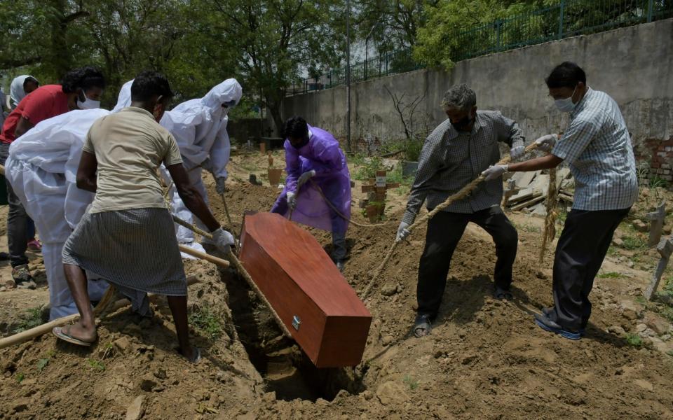 Family members, in protective suits, with the help of workers bury the body of a person who died of COVID-19, at a Christian cemetery in New Delhi, India, Saturday, May 29, 2021 - AP