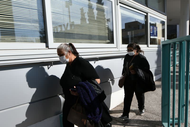 People wearing protective face masks sit outside the AHEPA hospital, where the first confirmed coronavirus case is being treated, in Thessaloniki