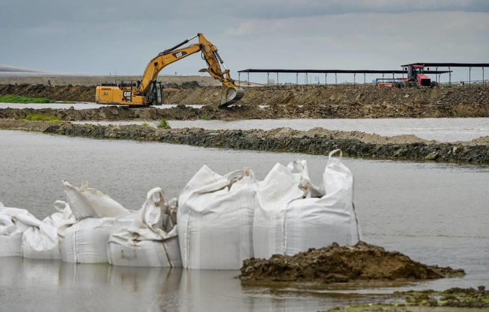 An excavator works to build a diversion berm to keep floodwater from a dairy in Kings County south of Hanford on Thursday, March 23, 2023.