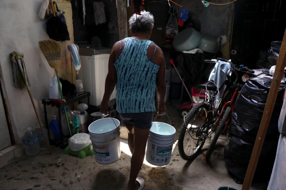 A woman carries buckets of non-potable water.