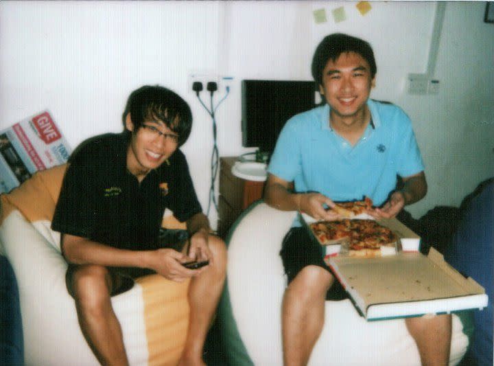 Pong of Give.Asia eating pizza with a friend, posing for a photo from a storeroom in NUS. 