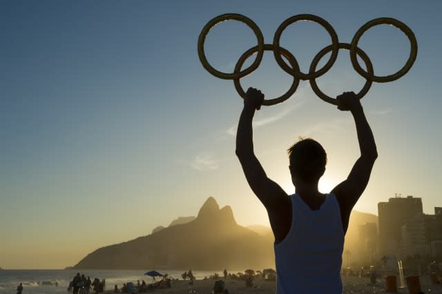 RIO DE JANEIRO, BRAZIL - MARCH 05, 2015: Athlete holding Olympic rings above sunset city skyline view of Two Brothers Mountain a