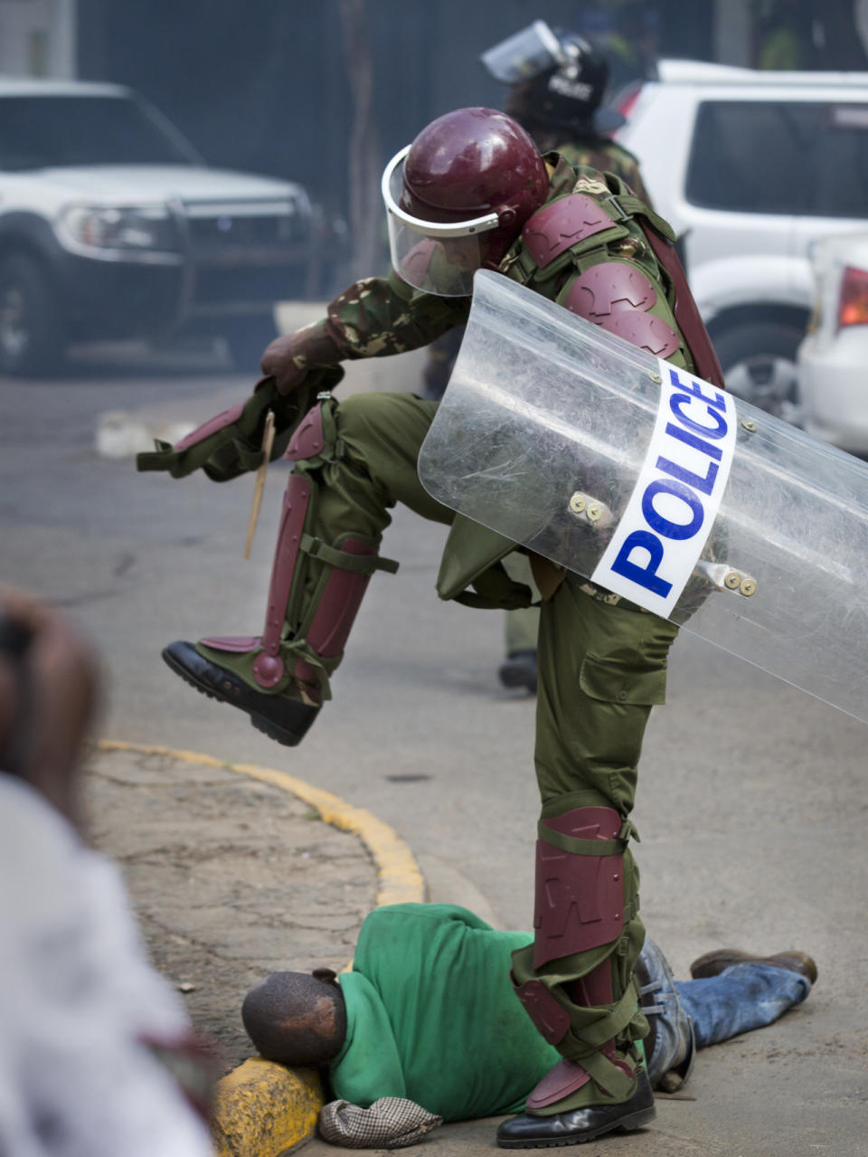 A Kenyan riot policeman prepares to kick a protester as he lies in the street after tripping over while trying to flee from officers during a protest in downtown Nairobi, Kenya, May 16, 2016. Kenyan police have tear-gassed and beaten opposition supporters during a protest demanding the disbandment of the electoral authority over alleged bias and corruption. (AP Photo/Ben Curtis)