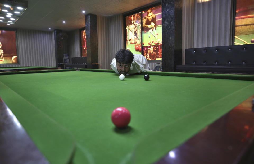 Mohammad Ikram plays snooker with his chin at a local snooker club in Samundri town, Pakistan, Sunday, Oct. 25, 2020. Ikram, 32, was born without arms, but everyone simply admires his snooker skills when he hits the cue ball with his chin and pots a colored ball on a snooker table. He lives in a remote rural town of Punjab province and his physical disability doesn't come in his way to fulfill his childhood dream of playing the game of snooker. (AP Photo/Anjum Naveed)