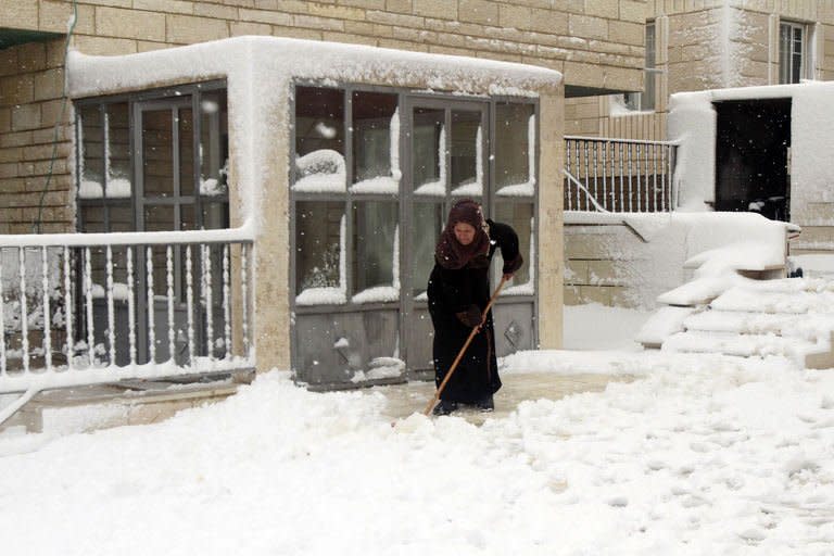 A Palestinian woman shovels in front of a building after heavy snowfall on January 10, 2013 in Tuqua, near the West Bank City of Bethlehem. The worst storms in a decade left swathes of Israel and Jordan under a blanket of snow and parts of Lebanon blacked out on Thursday, bringing misery to a region accustomed to temperate climates