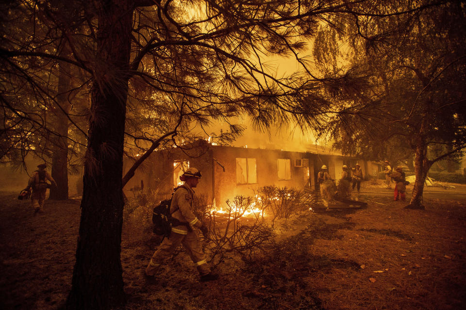 FILE - Firefighters work to keep flames from spreading through the Shadowbrook apartment complex as a wildfire burns through Paradise, Calif., on Nov. 9, 2018. Officials in Paradise began testing a new wildfire siren system this summer as the five-year anniversary of the deadly and devastating wildfire approaches. Reliable warning systems are becoming more critical during wildfires, especially as power lines and cell towers fail, knocking out communications critical to keeping people informed. (AP Photo/Noah Berger, File)