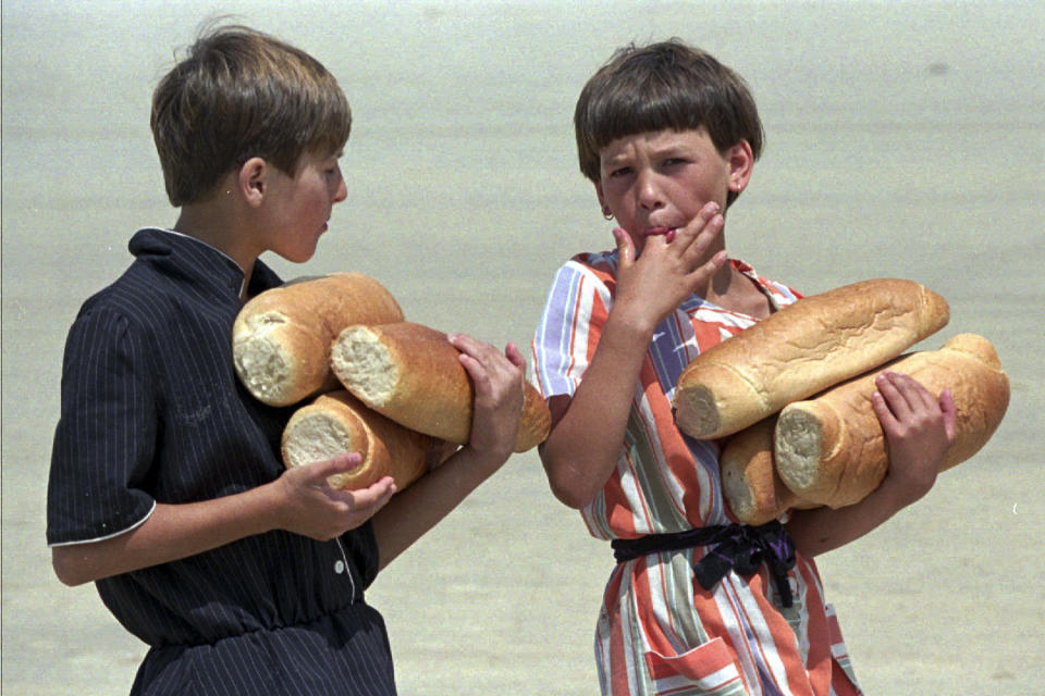 FILE- In this July 19, 1995, file picture, Bosnian refugee children from Srebrenica, carry loaves of bread, which they received from the United Nations at the refugee camp at Tuzla airport. Survivors of the genocide in the eastern Bosnian town of Srebrenica, mainly women, will on Saturday July 11, 2020, commemorate the 25th anniversary of the slaughter of their fathers and brothers, husbands and sons. The slaughter was the only atrocity of the brutal war that has been confirmed an act of genocide. (AP Photo/Michel Euler, File)