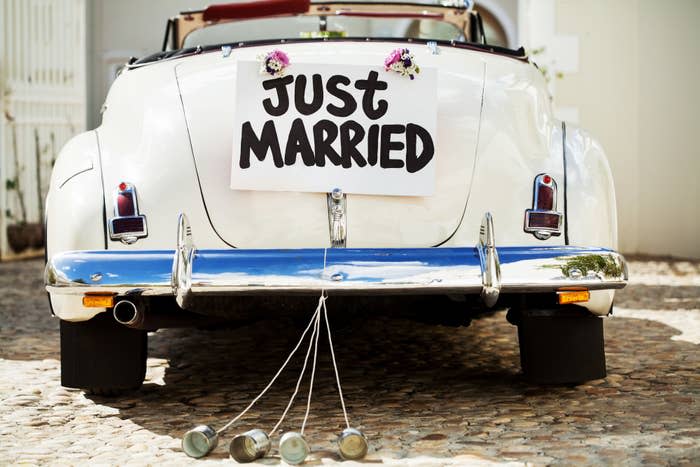 Classic convertible car with a "Just Married" sign on the back, adorned with flowers and trailing cans