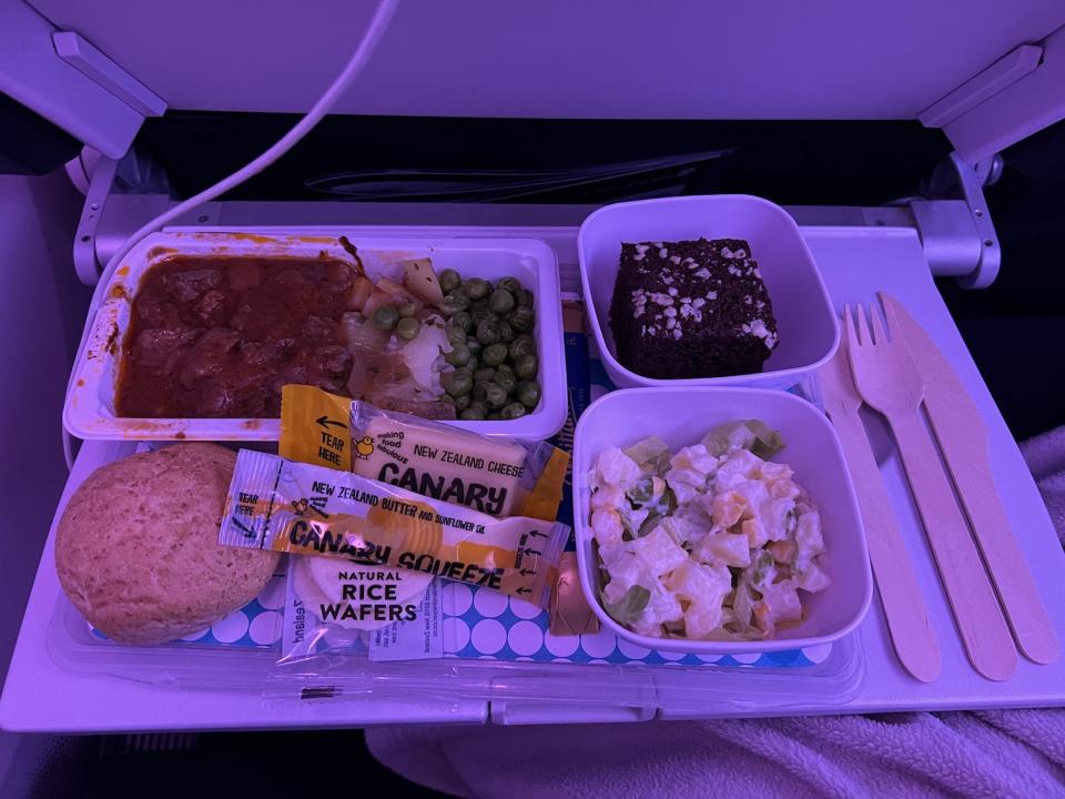 My meal on Air New Zealand with beef, peas, a chocolate dessert, bread, salad, and utensils.