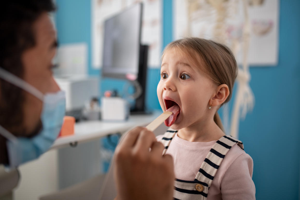 A zoung male doctor checking little girl's throat in his office.�