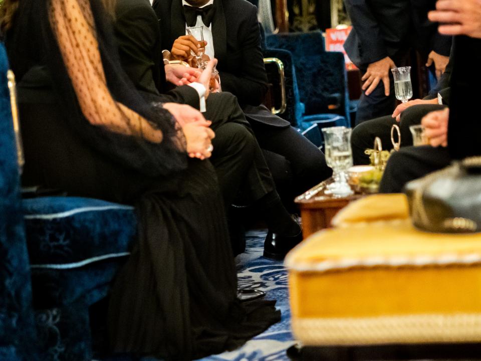 People dressed in black evening wear sit in blush, blue seats while drinking from champagne glasses