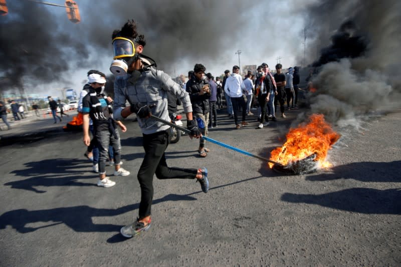 An Iraqi demonstrator pulls a burning tire during ongoing anti-government protests in Basra