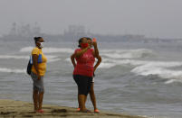 People take selfies with the Iranian oil tanker Fortune, in the background, docked at the El Palito refinery near Puerto Cabello, Venezuela, Monday, May 25, 2020. The first of five tankers loaded with gasoline sent from Iran is expected to temporarily ease Venezuela's fuel crunch while defying Trump administration sanctions targeting the two U.S. foes. (AP Photo/Juan Carlos Hernandez)