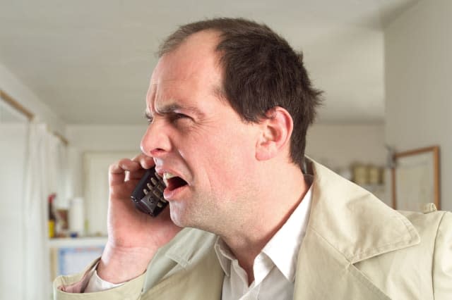 Mature man using mobile phone, indoors, frowning