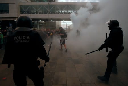 Police officers and protesters stand amid smoke during a demonstration at the airport, after a verdict in a trial over a banned independence referendum, in Barcelona