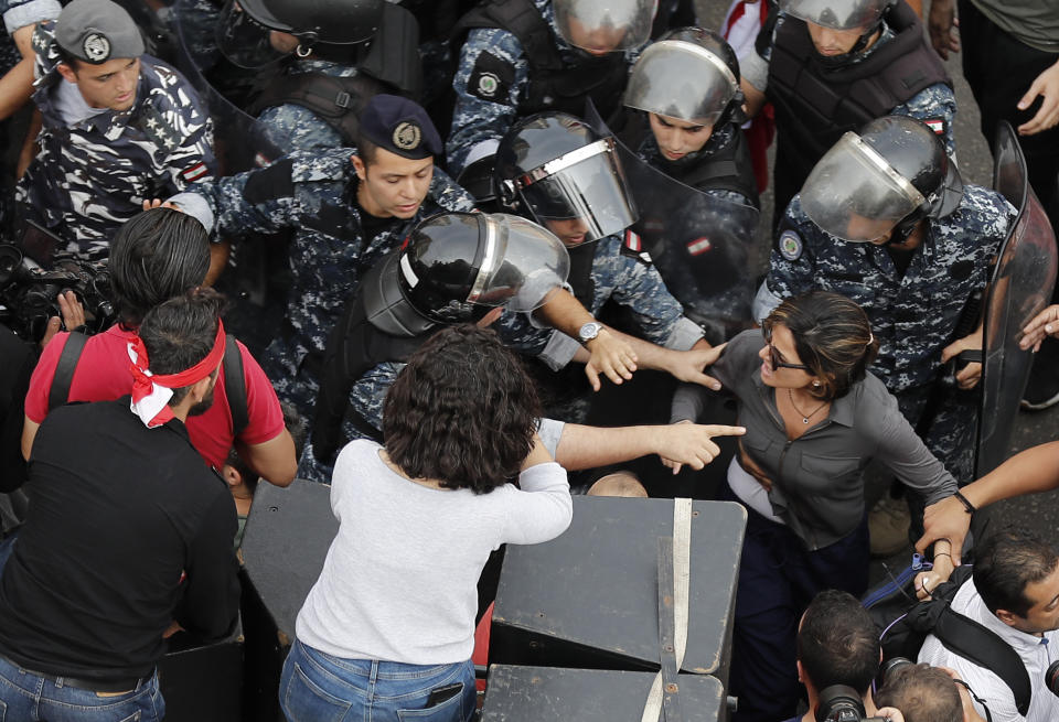 In this Friday Oct. 25, 2019, MTV television reporter Nawal Berry, right, is protected by riot policemen after she was attacked by Shiite supporters of Hezbollah and Amal Movement groups during an anti-government protest, in Beirut, Lebanon. Lebanese journalists are facing wide-ranging harassment and obstacles to their work - including verbal insults and physical attacks, even death threats - amid reporting on nearly 50 days of anti-government protests, drawing into question Lebanon’s reputation as a haven for free speech in a troubled region. (AP Photo/Hussein Malla)
