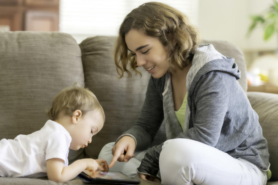 A girl and a young boy play with a tablet on a couch