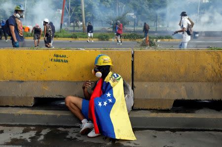 An opposition supporter wears a national flag of Venezuela over his shoulders as he takes cover during clashes with riot police forces at a rally against Venezuelan President Nicolas Maduro's government in Caracas, Venezuela June 22, 2017. REUTERS/Carlos Garcia Rawlins