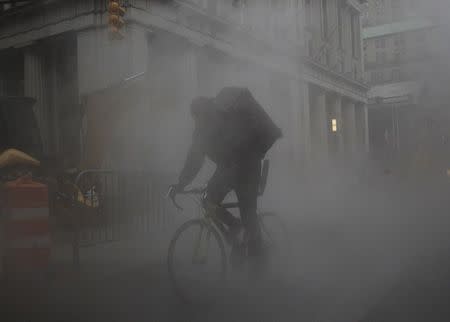 A bicycle messenger rides through a steam cloud in New York's financial district February 24, 2016. REUTERS/Brendan McDermid