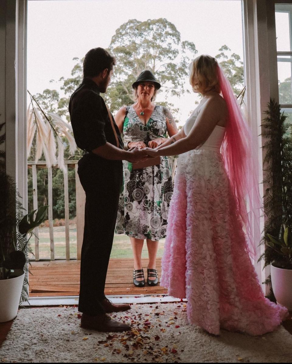 Pagel and her husband holding hands on their wedding day. Pagel is wearing a white dress with a white and pink skirt and a pink veil.