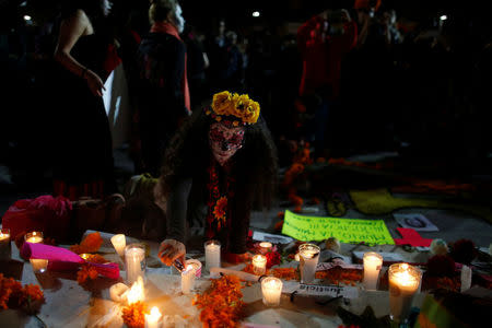 An activist with her face painted to look like the popular Mexican figure "Catrina" lights a candle to put it on an altar during a march against femicide during the Day of the Dead in Mexico City, Mexico November 1, 2017. Picture reads "Justice" REUTERS/Carlos Jasso