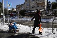 A woman pulls children on a sled on a snow-covered street in Jerusalem December 15, 2013. Jerusalem's heaviest snow for 50 years forced Israeli authorities to lift a Jewish sabbath public transport ban on Saturday and allow trains out of the city where highways were shut to traffic. REUTERS/Darren Whiteside (JERUSALEM - Tags: ENVIRONMENT SOCIETY)